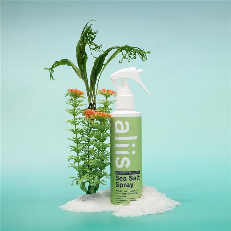 Bottle of Aliis sea salt spray with plants on a light blue background