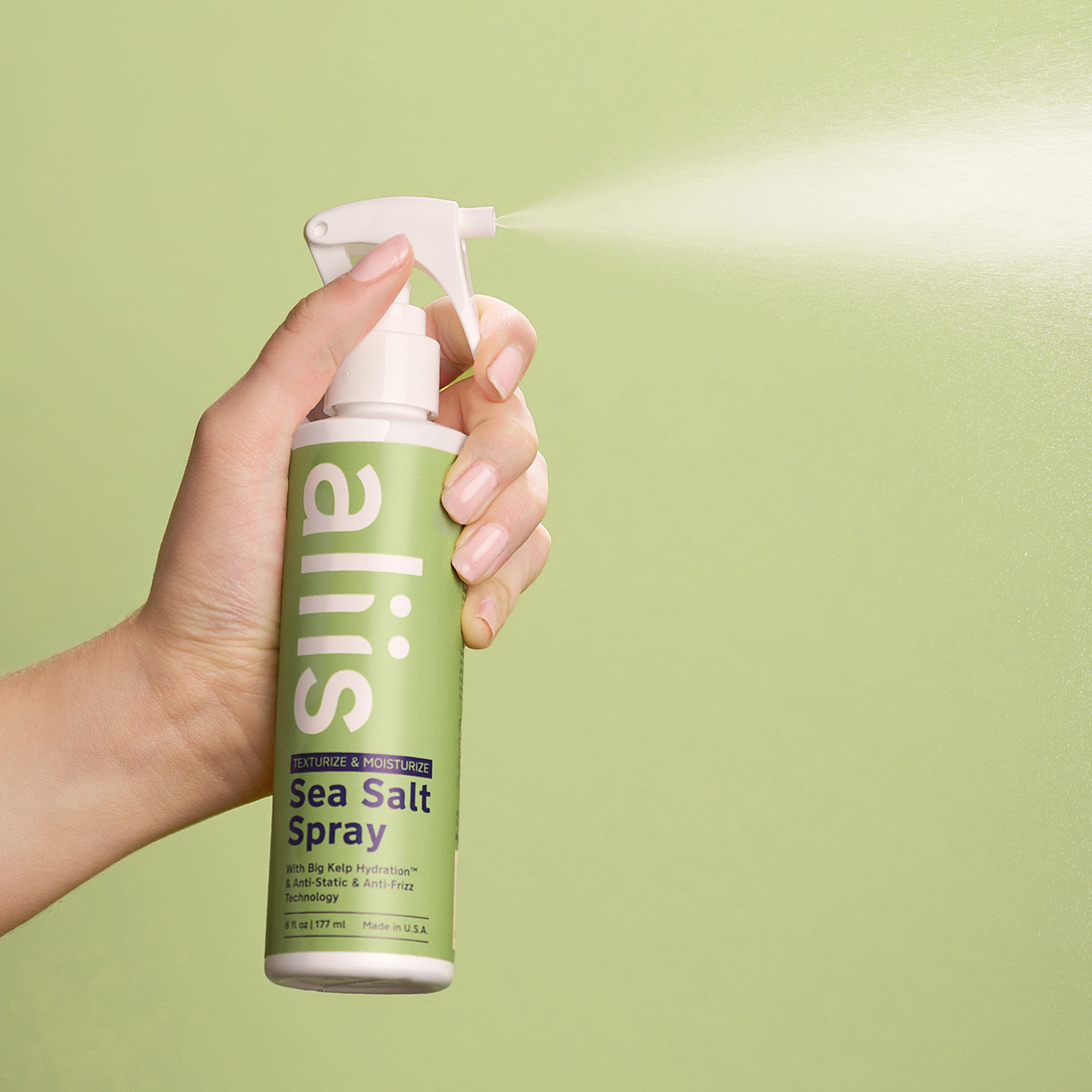 Hand holding a bottle of Aliis Sea Salt Spray against a green background