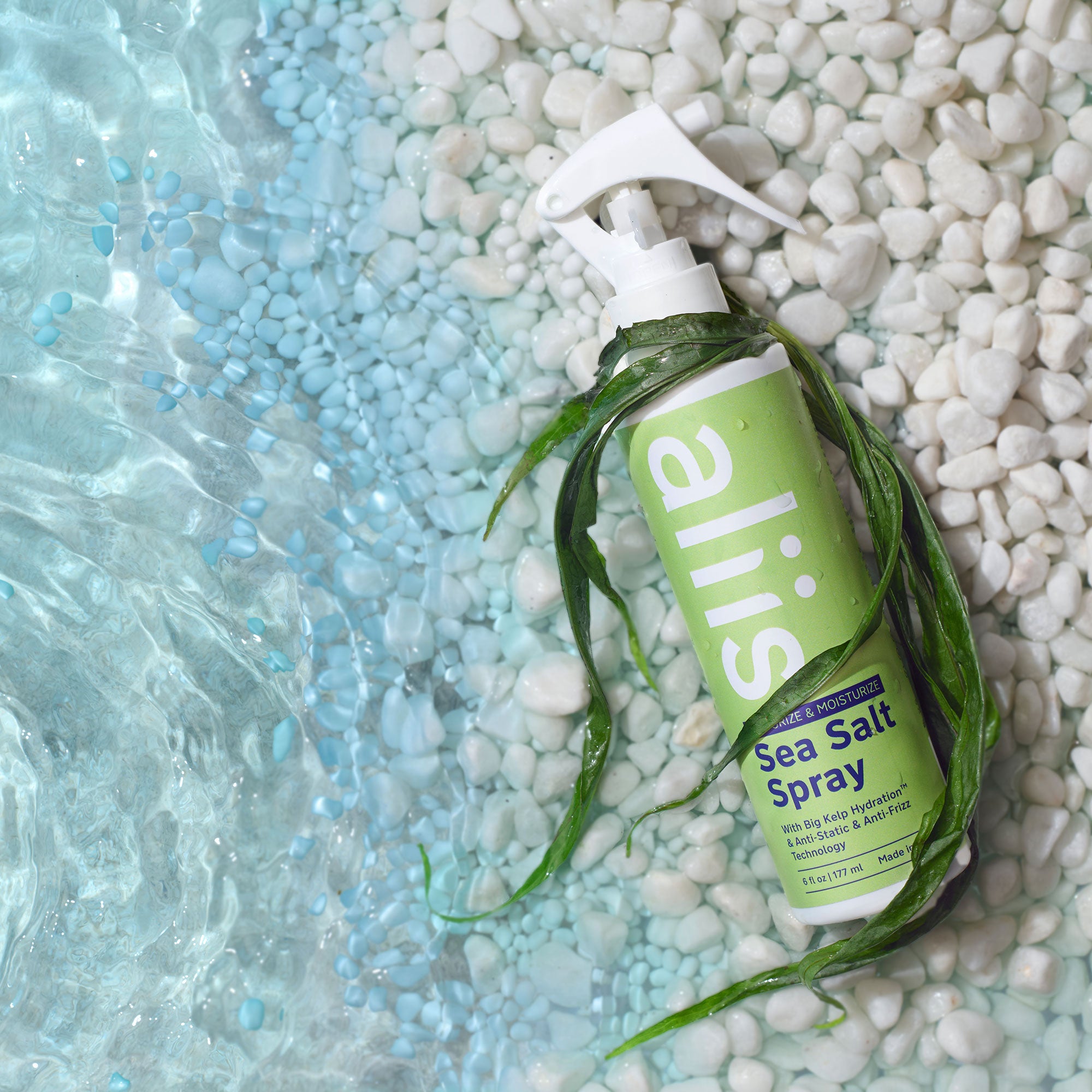 Green bottle of Aliis sea salt spray on pebbles with water in the background